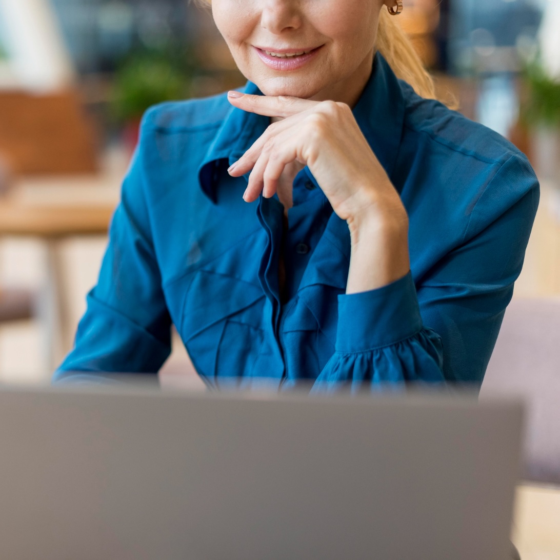 Working at a laptop Woman in a blue shirt smiling at a laptop screen